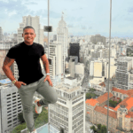 empresário Adriano de Barros numa sacada transparente com paisagem urbana ao fundo