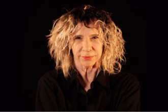 dramaturga Denise Stoklos olhando a câmera sobre fundo preto